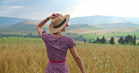 Inspired dreaming girl walking in the rural field against amazing horizon scenery. Young woman wanderer exploring virgin nature of Italian paradise Val d'Órcia, Tuscany in summer. Italy