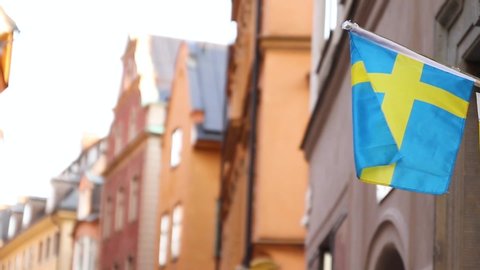 Real Swedish flags fly in the air outside. Flag Of Sweden on the background of the sky and flying clouds in the old town on the background of old houses