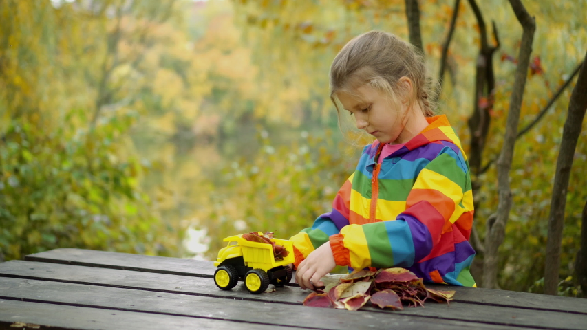 Little girl and boy play with toy car in autumn day. Cleaning of real leaves with a toy dump truck. The concept of cleanliness and order.