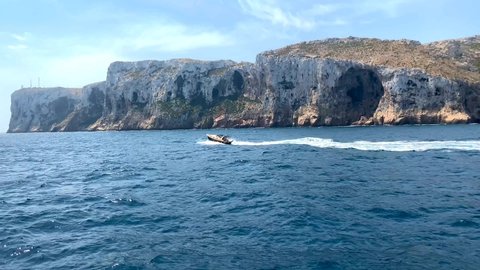 A boat sailing in the Mediterranean sea, near the Denia and Javea coast in Spain. The cliff of San Antonio Cape is in the background.