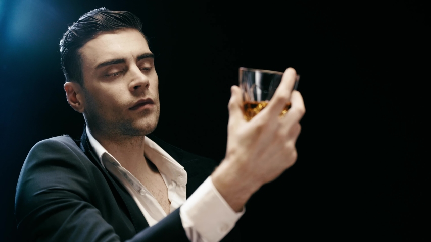 pensive businessman looking at glass of whiskey and drinking on black with smoke