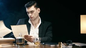 focused businessman doing paperwork, signing documents and drinking whiskey at table on black