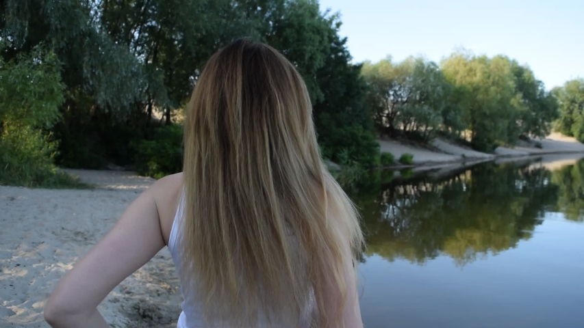 Portrait of a young brunette girl in a white t-shirt on the beach near the lake
