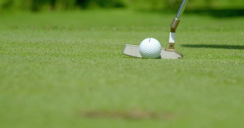 Close up of a golf ball putt dropping into the hole.  It shows the golf ball with an alignment marker to help the golfer line up the shot.