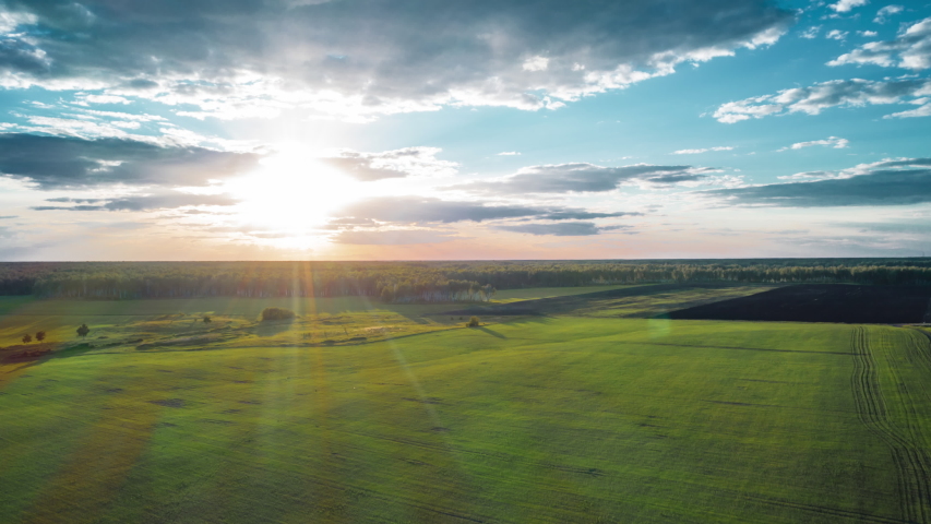 Beautiful sunset sky over a green meadows with mixed forest; agricultural fields with last sunlights shining through the clouds in summer evening; horizon line and sky gradient; countryside landscape Royalty-Free Stock Footage #1034156327