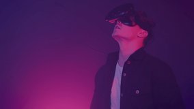 Young attractive man using modern virtual reality headset with gamepad on the neon lights background. Remote controllers, clicks, man work in VR, gesticulating by hands.