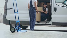delivery woman sitting in car and giving cardboard boxes to delivery man putting packages on metallic hand truck