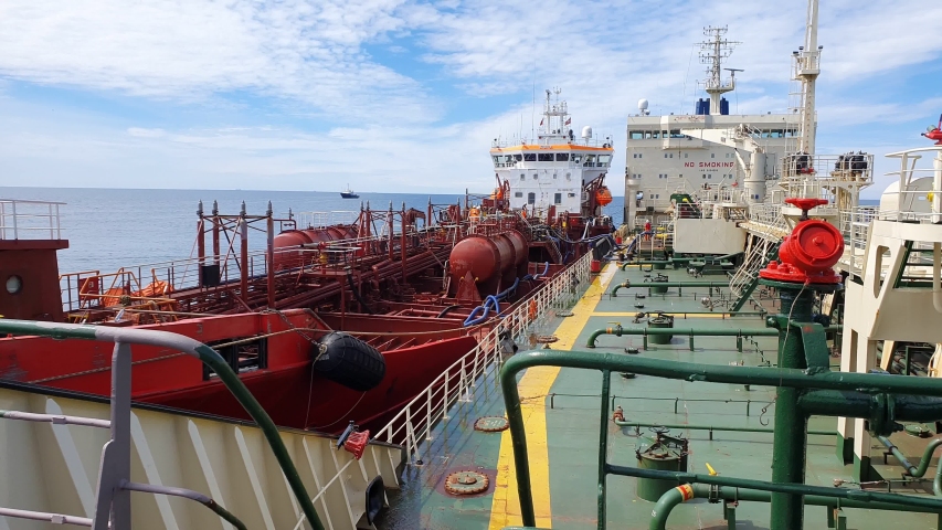 red and grey oil tankers with different modern pumping pipes drift closely side by side under blue cloudy sky