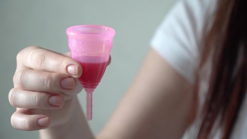 Close up of a young woman hand holding reusable silicone menstrual cup with blood. Zero waste menstruation hygiene concept. Ecological alternative for periods.