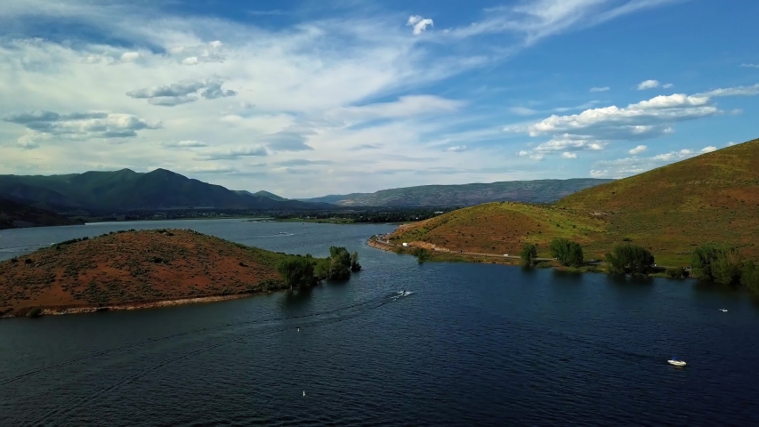 Beautiful landscape view of Deer Creek Reservoir in Heber Valley Utah with speed boats and jet skis on the lake on a cloudy summer day.