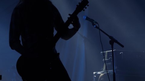 Silhouette of electric bass guitar player. Silhouette of bass electric guitar player on the stage with microphone and bright warm illumination, live music theme