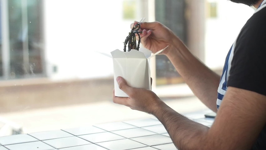 Young bearded arabic or latin young man eating street food, Chinese noodles