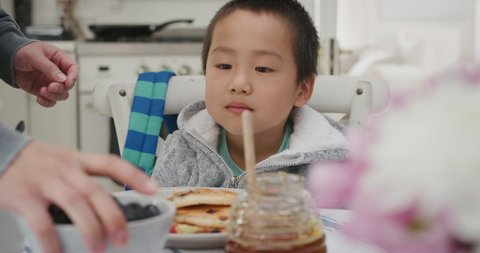 cute little Japanese boy eating fresh waffles for breakfast enjoying delicious homemade meal with family in kitchen at home 4k