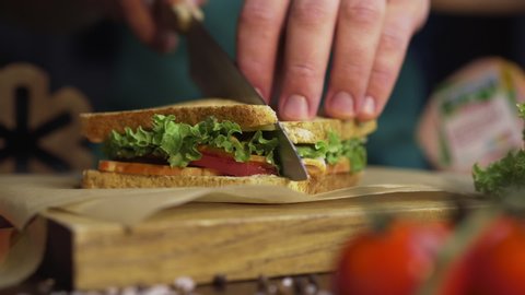 Man cuts club sandwich in a half by sharp knife on a wooden board at the kitchen, making of the fastfood at home, chef is cooking sandwich, Full HD Prores HQ 422