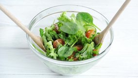 Cropped view of woman mixing vegetable salad in bowl with wooden spatulas