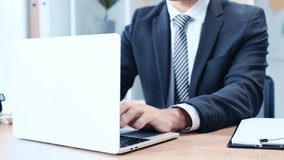 cropped view of businessman using laptop while sitting at workplace in office