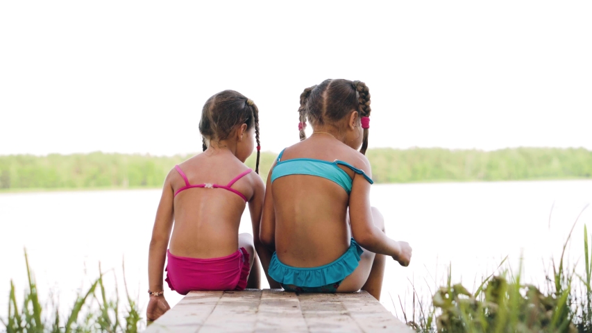 Two sisters sit on the river Bank on the bridge