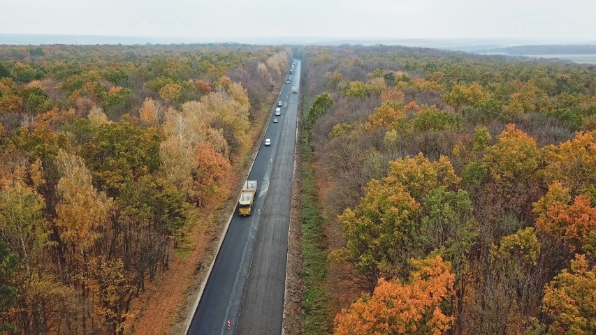 Aerial view of autumn road with cars. Many cars are moving on one side of the road in autumn forest. Camera moves right.