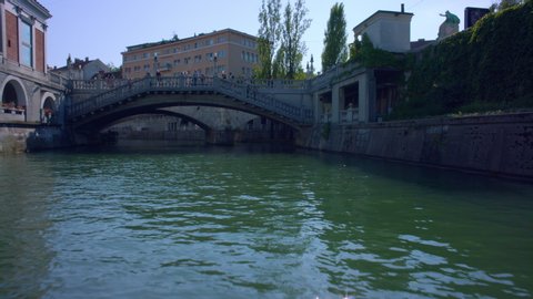 View from a boat on a river in Slovenia's capital Ljubljana. Urban setting on a summer day. Going under famous bridges, old city architecture. 