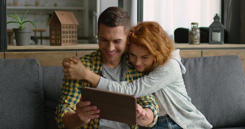 Young man and woman found a product they like in online store, using their tablet, woman is hugging man, being surprised, saying wow, smiling, sitting on a couch. 4K, shot on RED camera.