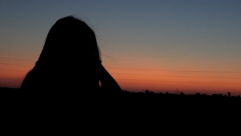 4k. Ultra HD. Silhouette of young woman with hair moving in the wind. The female silhouette over a beautiful sunset. Girl waiting for the moment, looking at the horizon.