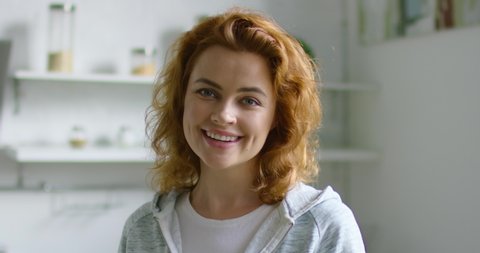 Portrait of young happy woman standing in the kitchen, smiling, looking at camera, full of positive emotions and joy, enjoying her life, red curly hair, blue eyes, Caucasian. 4K, shot on RED camera.