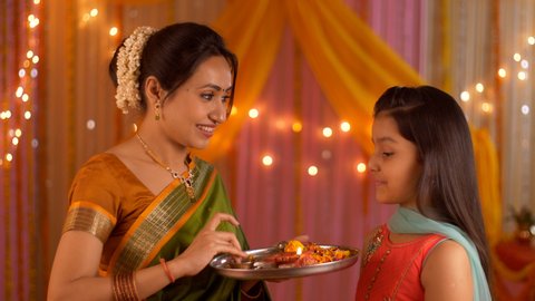 Mother putting tilak on young daughter's forehead - Celebration at home. Festive colorful background. Indian stock footage of nuclear family celebrating Diwali festival at home - Mother-daughter pe...