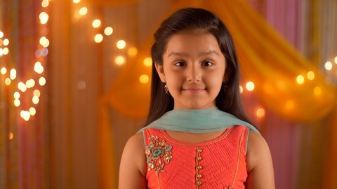 Young girl wearing salwar kameez smiling at the screen - Headshot. HD video clip of a smiling girl - wearing ethnic clothes for puja at home. Colorful festive background with lights
