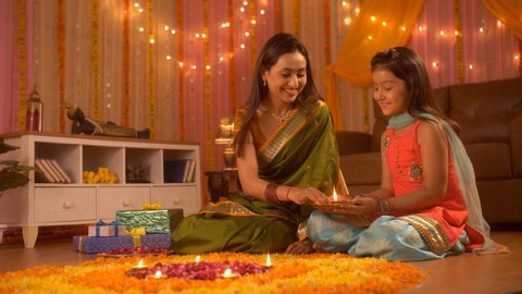 Beautiful and loving mother and daughter decorating flower's rangoli with Diyas - Festival. Indian Stock Footage of mother and daughter - sitting on the floor and decorating house for Diwali festival