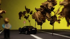 Video of a man sitting next to his broken, black, car figurine in the middle of a highway model next to trees made from small branches.