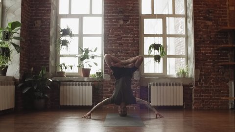 Hand standing pose. Young sporty man doing yoga in studio with wooden floor and big windows. Freedom, health and yoga concept with copy space. Stockvideó