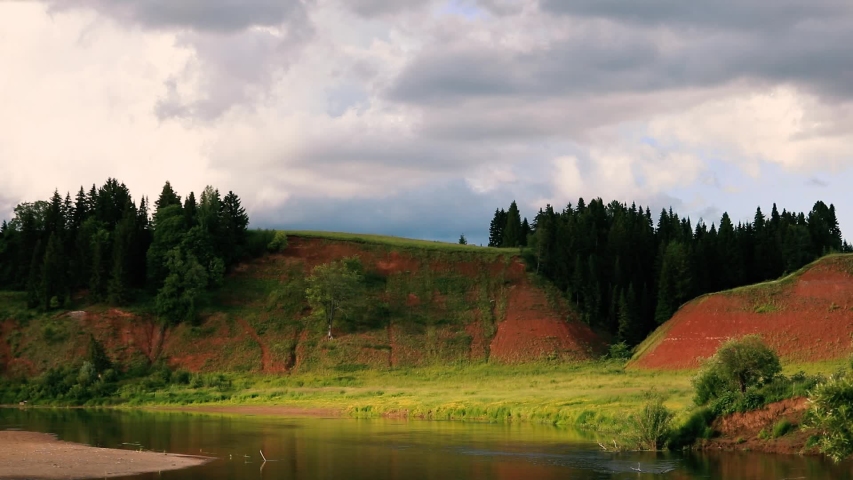 Clouds run across the blue sky. Time lapse. Below the river flows and the forest grows