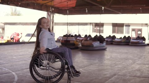 Young disabled invalid handicapped woman dancing in in wheelchair on the electric cars attraction surface