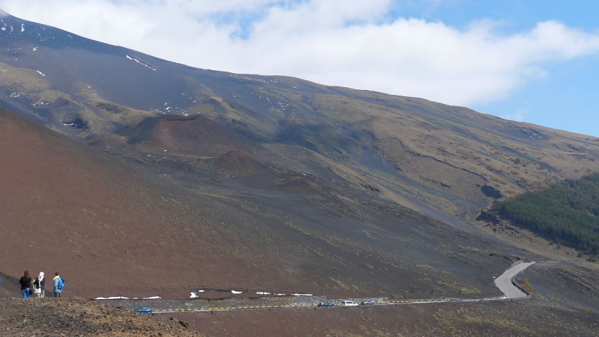 Panning shot of volcanic scenery of south side of mountain Etna,famous volcano in Europe.Cars driving road SP92 near Rifugio Sapienza refuge,man standing at the top of Silvestri crater (end of clip).
