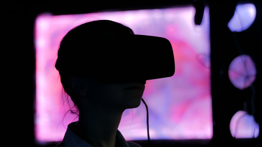 Woman using virtual reality headset and looking around at interactive technology exhibition with changing multi color light illumination. VR, augmented reality, immersive and entertainment concept | Shutterstock HD Video #1034227280