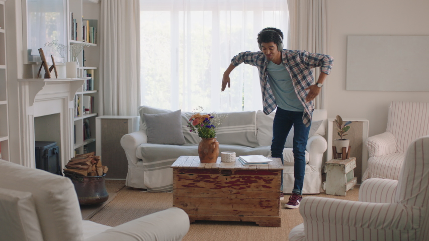 Happy young man dancing at home celebrating success listening to music wearing headphones having fun dance in living room on weekend | Shutterstock HD Video #1034230154