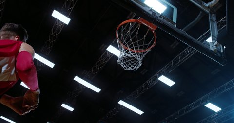 Low angle of professional basketball player in action performing slam dun in a basketball hoop on a sports arena