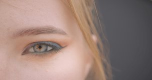 Closeup half face portrait of young pretty caucasian female face with eye looking at camera with background isolated on gray