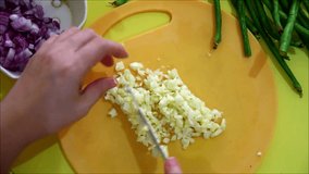 Overhead or flatlay steady video shot of a person mincing garlic with a knife on a chopping board