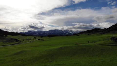 Beautiful rising drone shot over green pastures and snowy mountains.