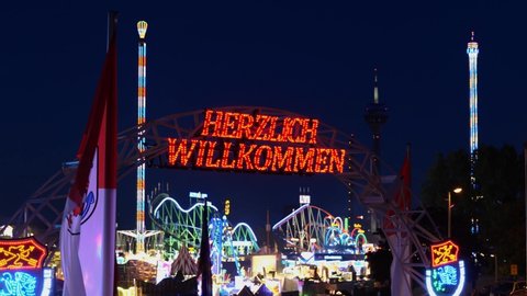 Düsseldorf, Germany - JULY 2019: Herzlich Willkommen or Warm Welcome led sign at gate of Rheinkirmes amusement park, and blur background colourful illuminating of amusement rides during night time.