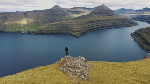 Flying around a hiker at the summit of a mountain above Funningur on Faroe Islands who enjoys spectacular views over faroese fjords. 4K UHD video.