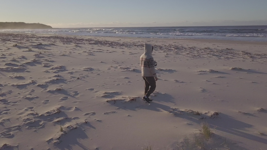 Aerial view of a man dramatically walking on a lonely empty sand beach in Australia at sunset.