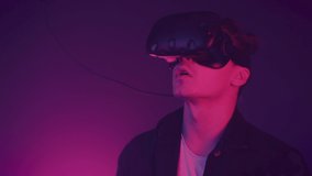 Young attractive man using modern virtual reality headset with gamepad on the neon lights background. Remote controllers, clicks, man work in VR, gesticulating by hands.