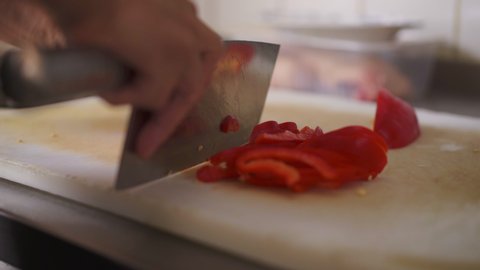 Close up front angle shot of a chef cutting red peppers with cleaver knife