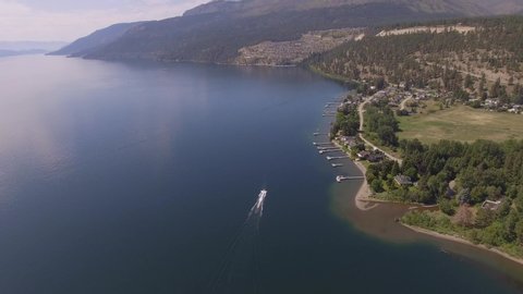Following aerial of a boat motoring past a small lake-side community