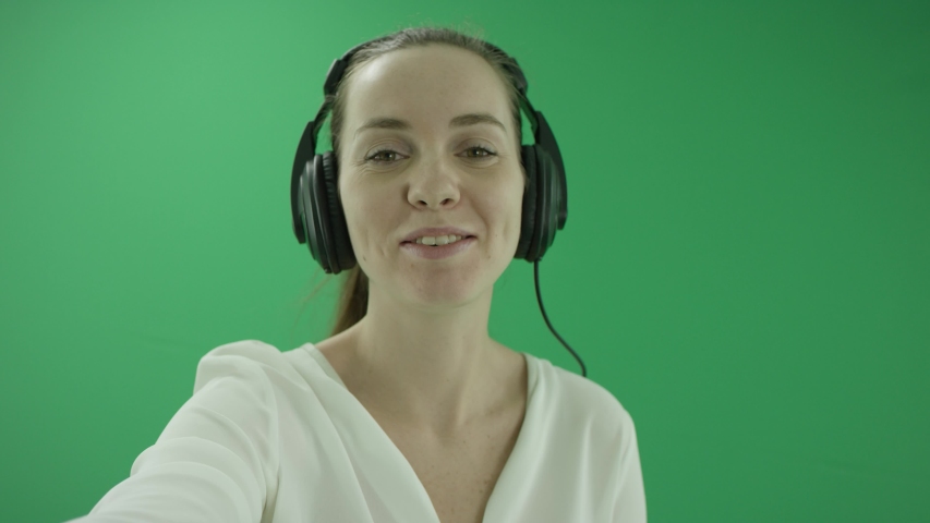 Happy businesswoman listening to music in the headphones and dancing . She wears formal dress: white shirt and blak skirt, standing in close up in the centre the greenscreen
