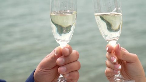 Man and woman clinking glasses of sparkling champagne against flowing water background. Closeup of glasses and hands