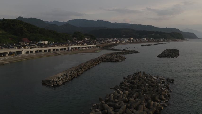 Japan coastline harbour waterfront aerial flyover during sunset over calm ocean waters.