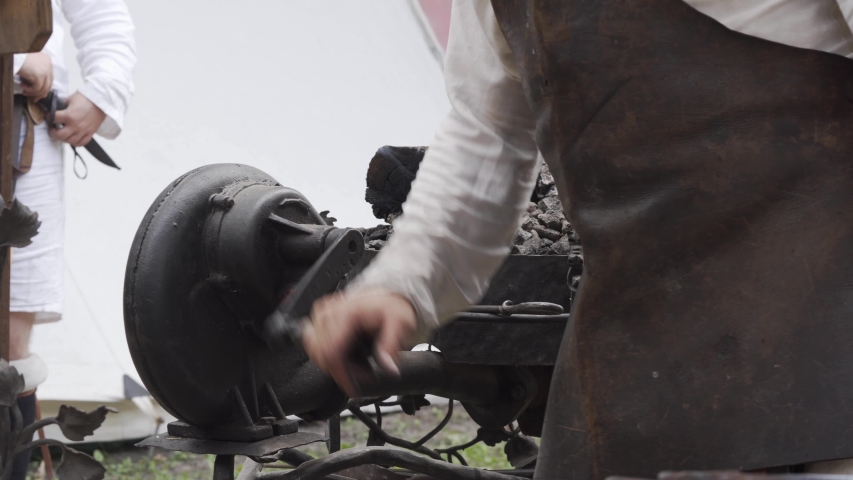 Blacksmith turning handle of hand-cranked blower to push air to forge. Slavic and old culture days in Sobotka, Poland.